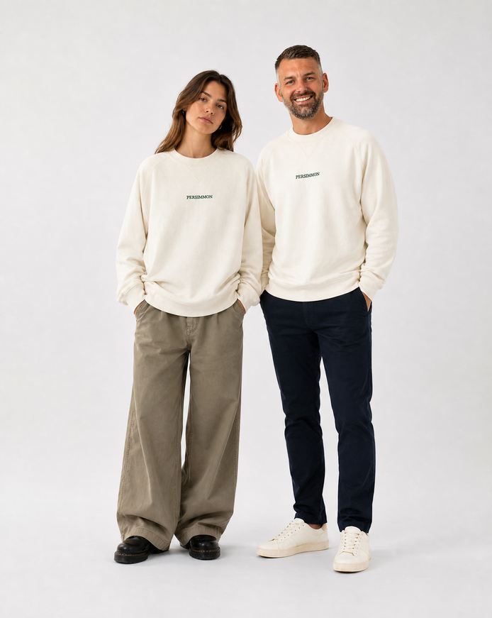Two people wearing matching cream sweatshirts with a logo on a white background