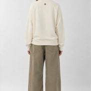 Person wearing a cream sweatshirt and beige pants on a white background