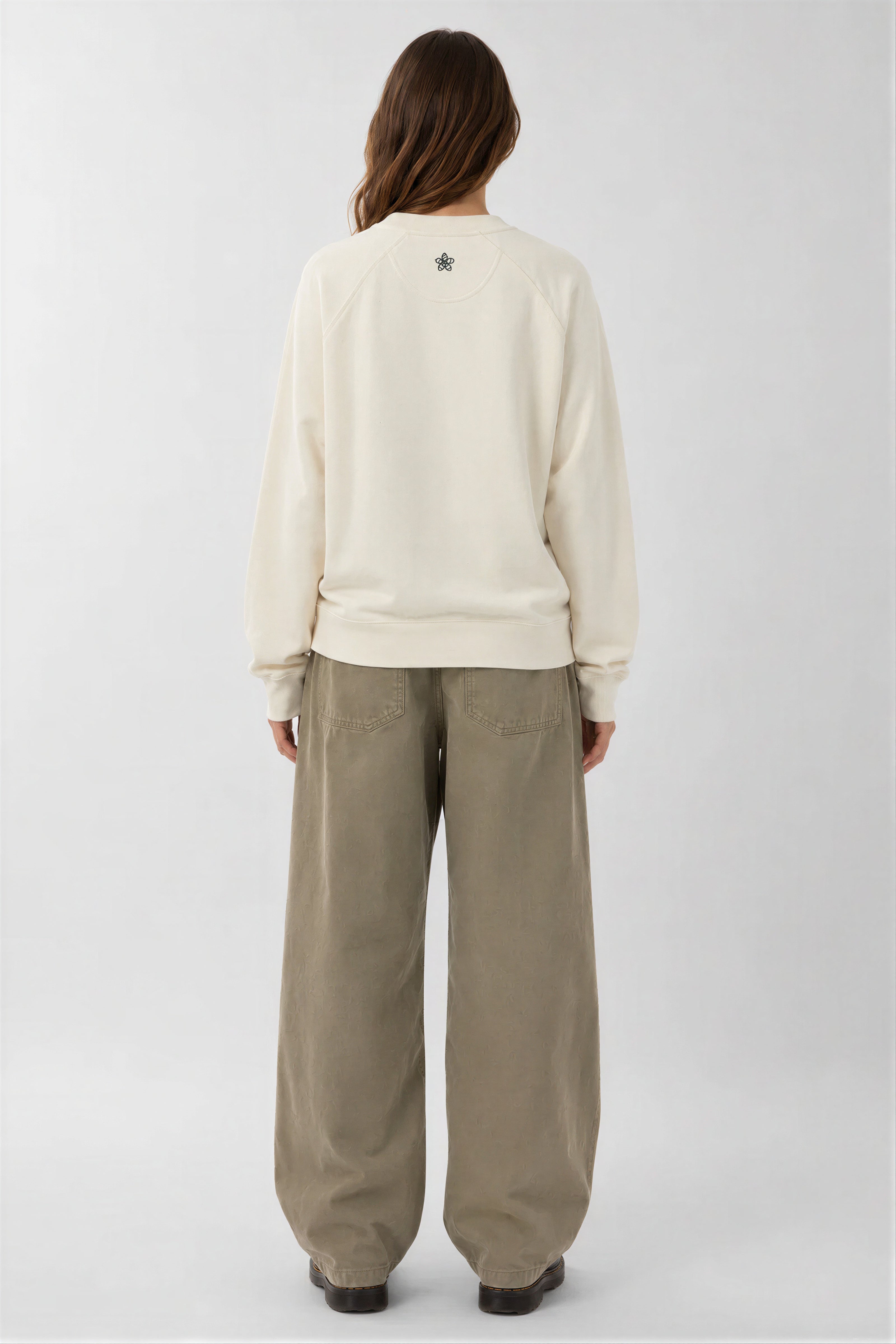 Person wearing a cream sweatshirt and beige pants on a white background