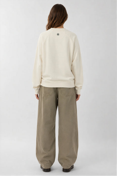 Person wearing a cream sweatshirt and beige pants on a white background