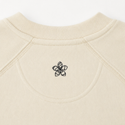 Close-up of a creamsweater with a dark green Persimmon logo on the neckline.