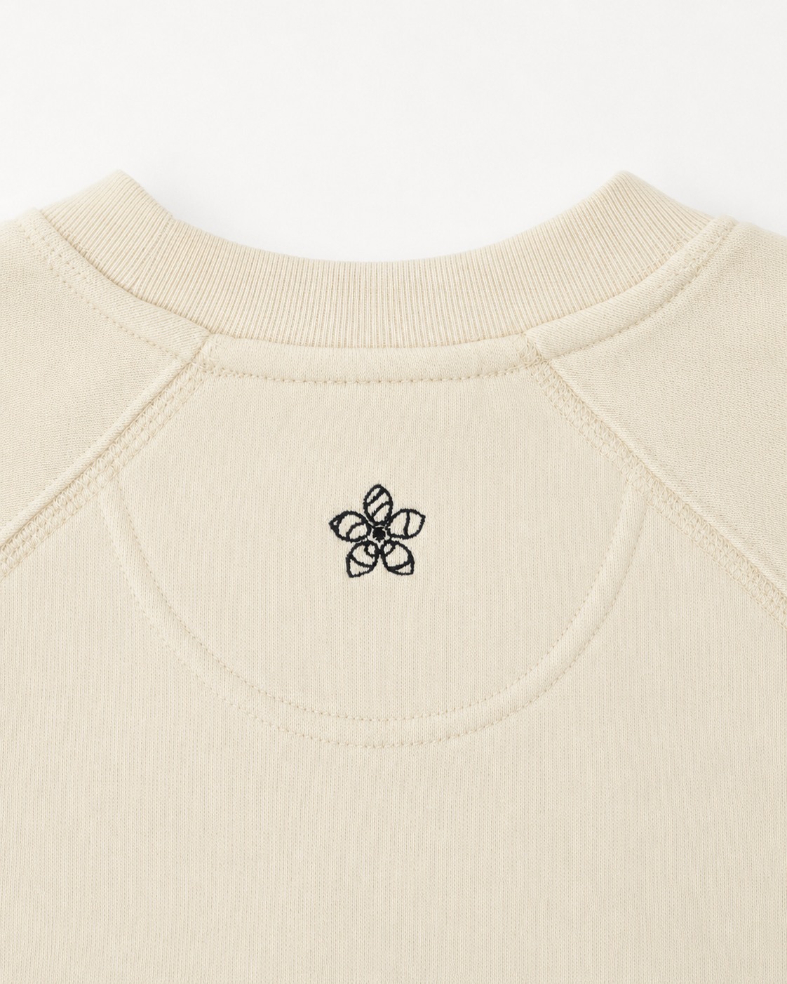 Close-up of a creamsweater with a dark green Persimmon logo on the neckline.