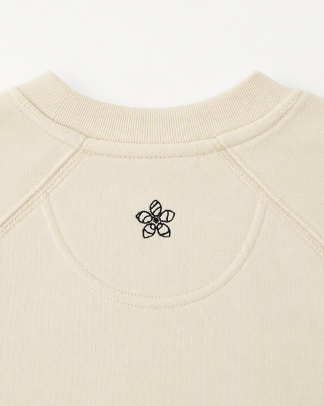 Close-up of a creamsweater with a dark green Persimmon logo on the neckline.