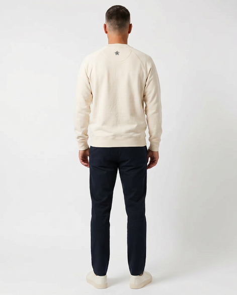 Man wearing a cream sweater and navy pants on a white background