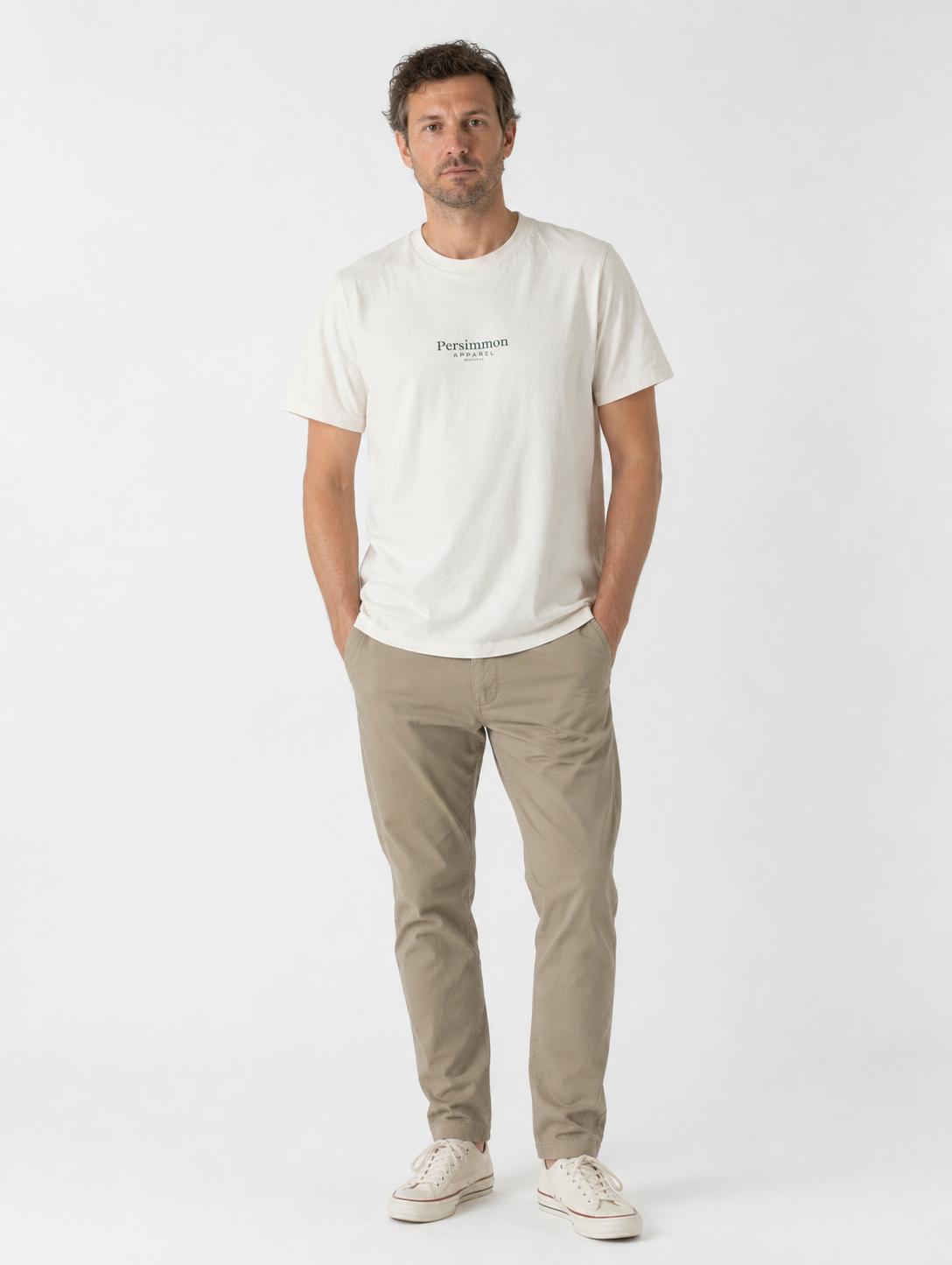 Man wearing a cream t-shirt with Persimmon Apparel branding and beige pants on a white background