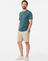 Man wearing a green t-shirt and beige shorts on a white background