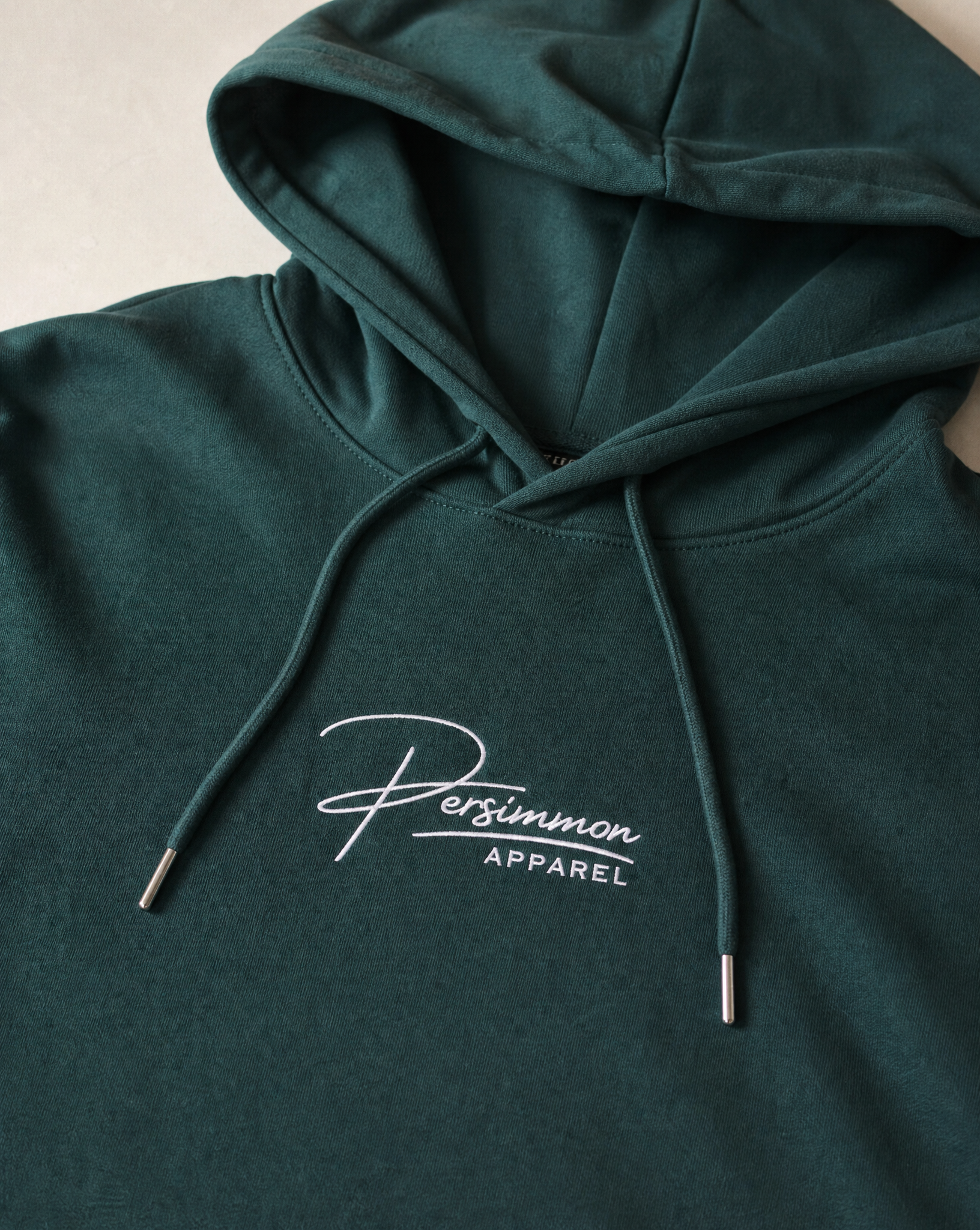 Green hoodie with 'Persimmon Apparel' logo on a neutral background